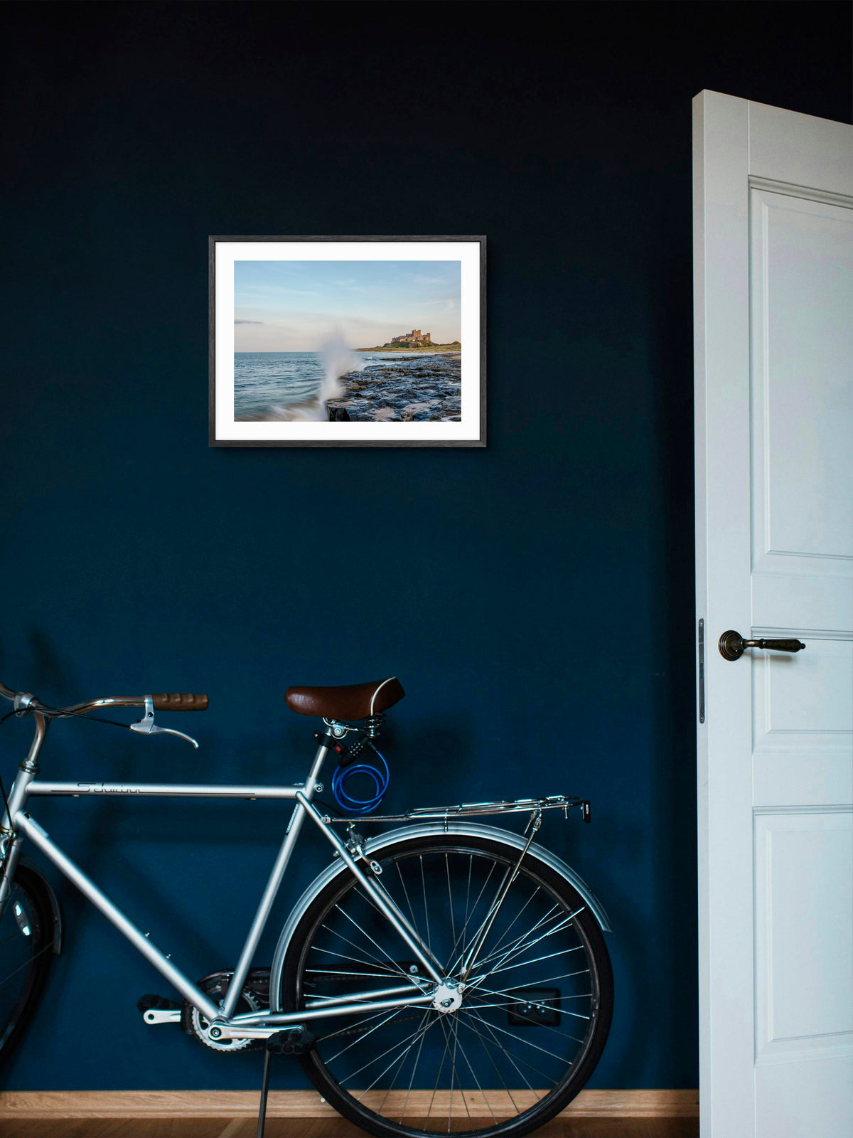 Waves crashing on rocks below Bamburgh Castle wall art displayed in a styled room setting.