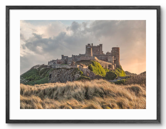 Bamburgh Castle beyond grass-covered dunes shown as a framed photographic print.