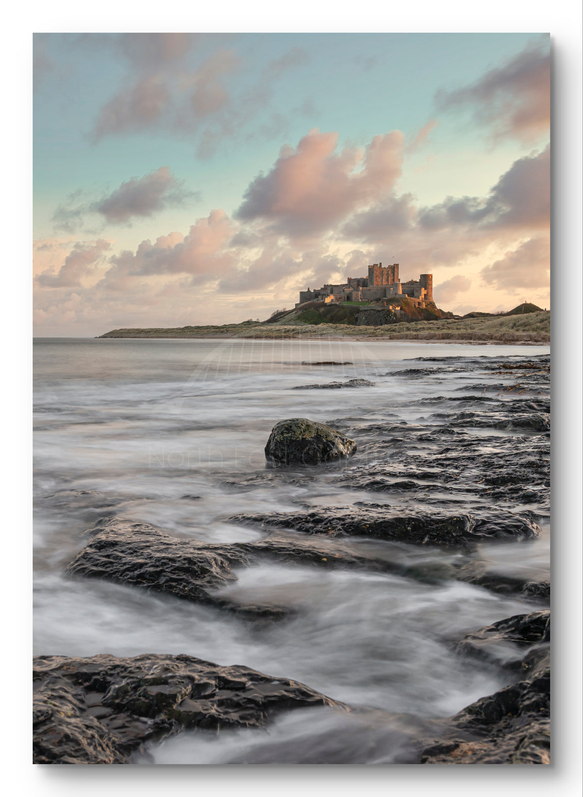 Waves on rocks at sunset near Bamburgh Castle shown as a canvas print.
