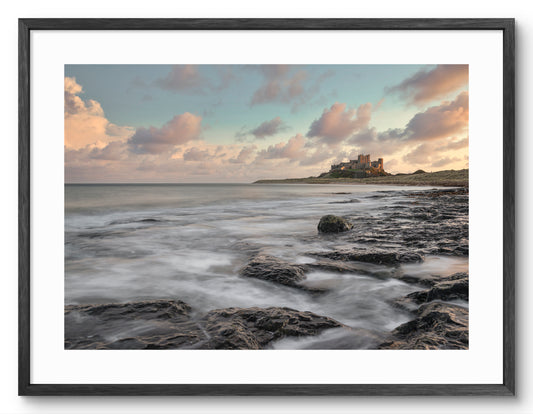 Waves on rocks below Bamburgh Castle shown as a framed photographic print.