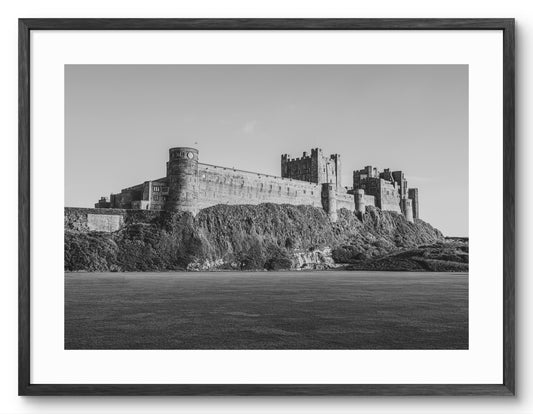 Black-and-white Bamburgh Castle from the cricket field shown as a framed photographic print.