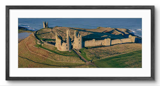 Dunstanburgh Castle Aerial View panoramic print — black frame and white mount