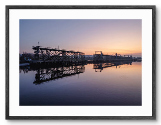 Dunston Staiths reflected in the River Tyne at sunset shown as a framed photographic print.