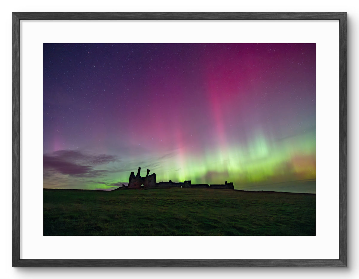 Northern Lights above Dunstanburgh Castle shown as a framed photographic print.
