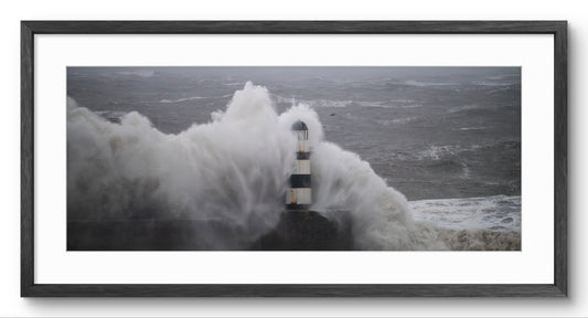 Seaham Lighthouse engulfed by a storm wave, in a black wooden panoramic frame with a white mount.