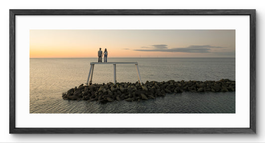 The Couple Sculpture at Sunset Panoramic Framed Print — black frame and white mount