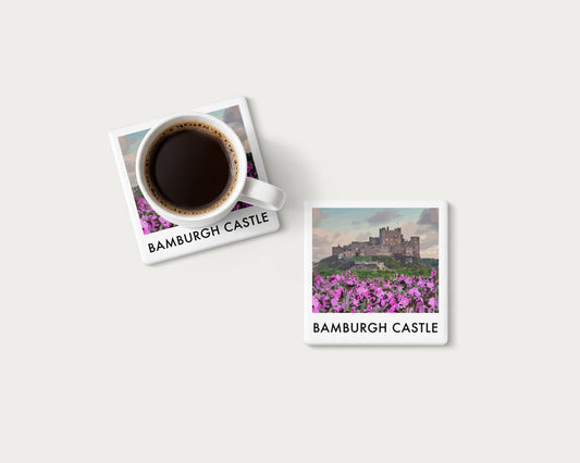 Illustrated ceramic coaster showing Bamburgh Castle with pink flowers in the foreground; mockup with a coffee mug.