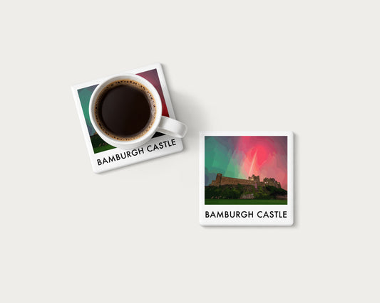 Illustrated ceramic coaster showing Bamburgh Castle beneath red and green aurora; mockup with a coffee mug.