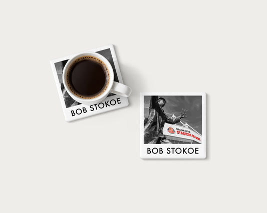 Illustrated ceramic coaster showing the Bob Stokoe statue in monochrome with red details; mockup with a coffee mug.