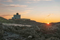 Lighthouse on a rocky island with a sunset in the background