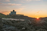 Lighthouse on a rocky island with a sunset in the background