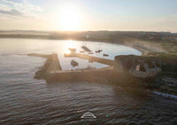 Sunset over a coastal area with boats and a fortification.