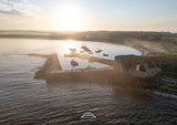 Sunset over a coastal area with boats and a fortification.