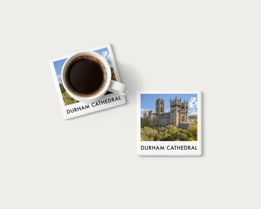 Illustrated ceramic coaster showing Durham Cathedral above autumn foliage beneath blue sky; mockup with a coffee mug.