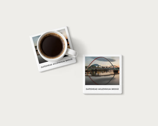 Illustrated ceramic coaster showing Gateshead Millennium Bridge and its reflection at dusk; mockup with a coffee mug.