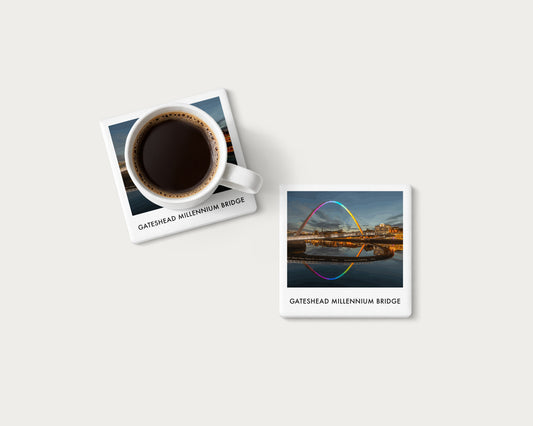 Illustrated ceramic coaster showing rainbow lights reflected beneath Gateshead Millennium Bridge; mockup with a coffee mug.