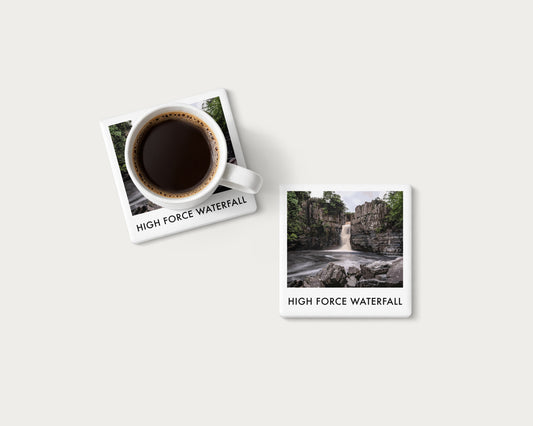 Illustrated ceramic coaster showing High Force waterfall cascading between rocky cliffs; mockup with a coffee mug.