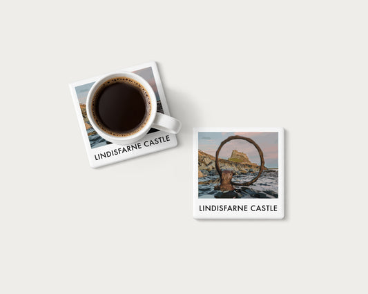 Illustrated ceramic coaster showing Lindisfarne Castle framed by an iron mooring ring; mockup with a coffee mug.