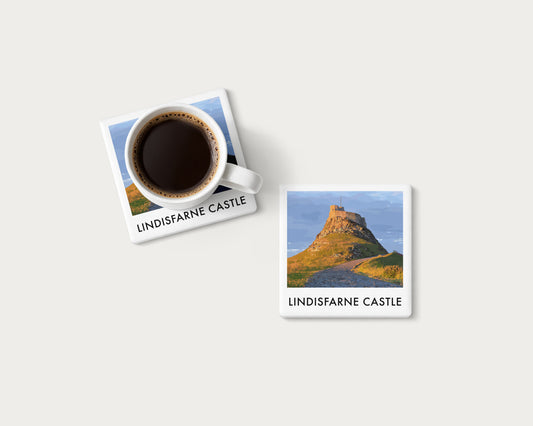 Illustrated ceramic coaster showing the path to Lindisfarne Castle in golden light; mockup with a coffee mug.