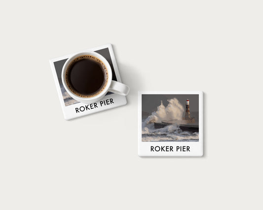 Illustrated ceramic coaster showing a large wave breaking beside Roker Pier lighthouse; mockup with a coffee mug.