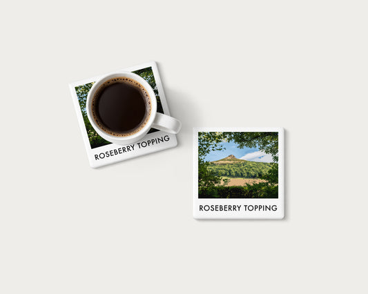 Illustrated ceramic coaster showing Roseberry Topping framed by leafy branches; mockup with a coffee mug.