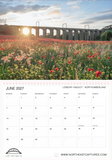 A printed calendar page for June 2027 with a large landscape photograph of the Lessbury Viaduct in Northumberland over a field of red and white flowers. The top portion shows the scenic landscape with warm sunlight, and the bottom portion contains the calendar grid, location text, and the website www.