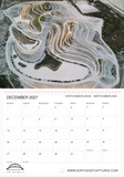 A printed calendar page for December 2027 with a large aerial landscape photograph of terraced earth mounds at the top and a grid of days at the bottom. Visible text includes NORTHUMBERLANDIA - NORTHUMBERLAND and the website www.