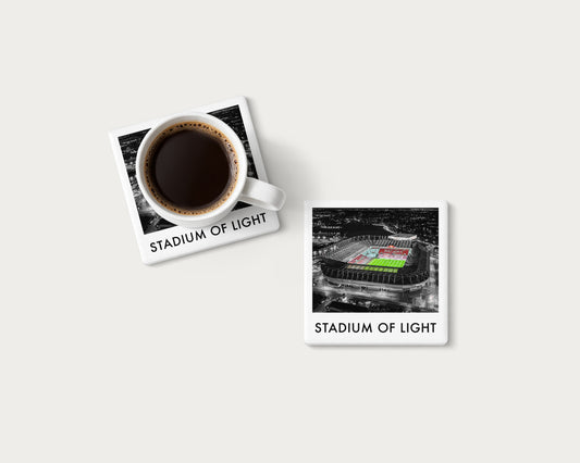Illustrated ceramic coaster showing an aerial Stadium of Light view with a green pitch and red seats; mockup with a coffee mug.