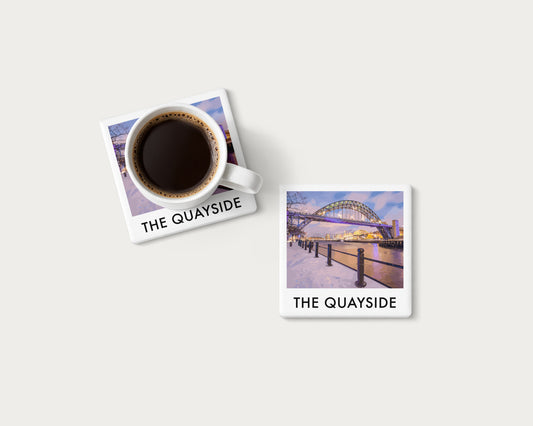 Illustrated ceramic coaster showing snow along Newcastle Quayside beneath the Tyne Bridge; mockup with a coffee mug.