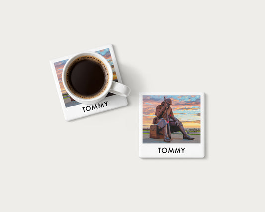 Illustrated ceramic coaster showing the Tommy statue in Seaham beneath colourful clouds; mockup with a coffee mug.