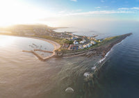 Aerial view of a coastal town with houses and a pier, surrounded by water.