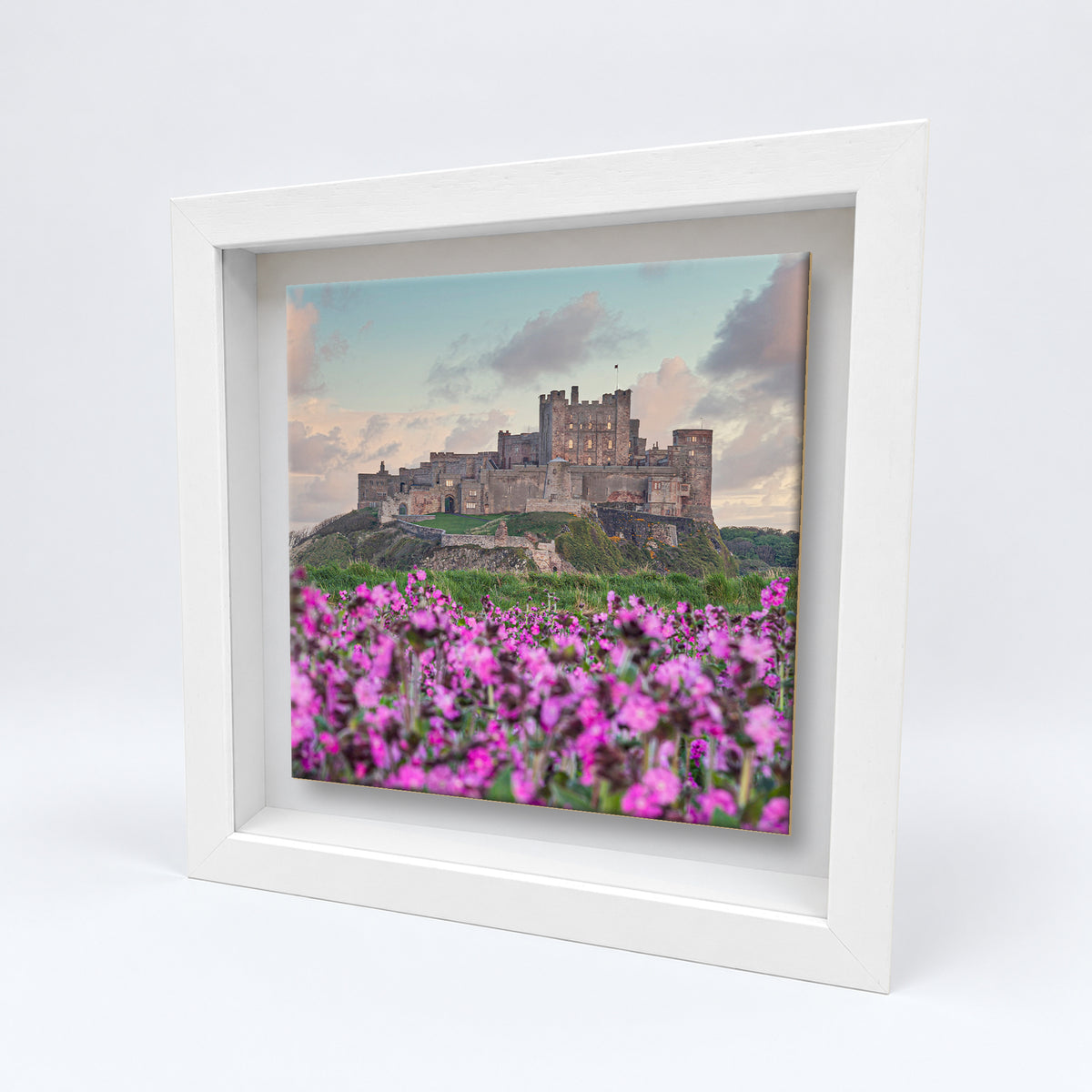 Bamburgh Castle and Flowers on an 8×8 inch ceramic tile in a white box frame, angled view