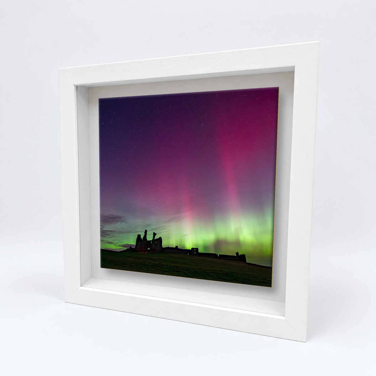 Dunstanburgh Castle Northern Lights on an 8×8 inch ceramic tile in a white box frame, angled view